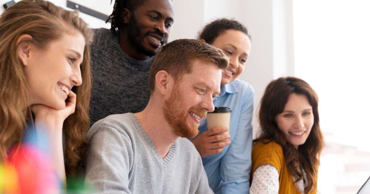 group of happy colleagues hovering around a laptop 